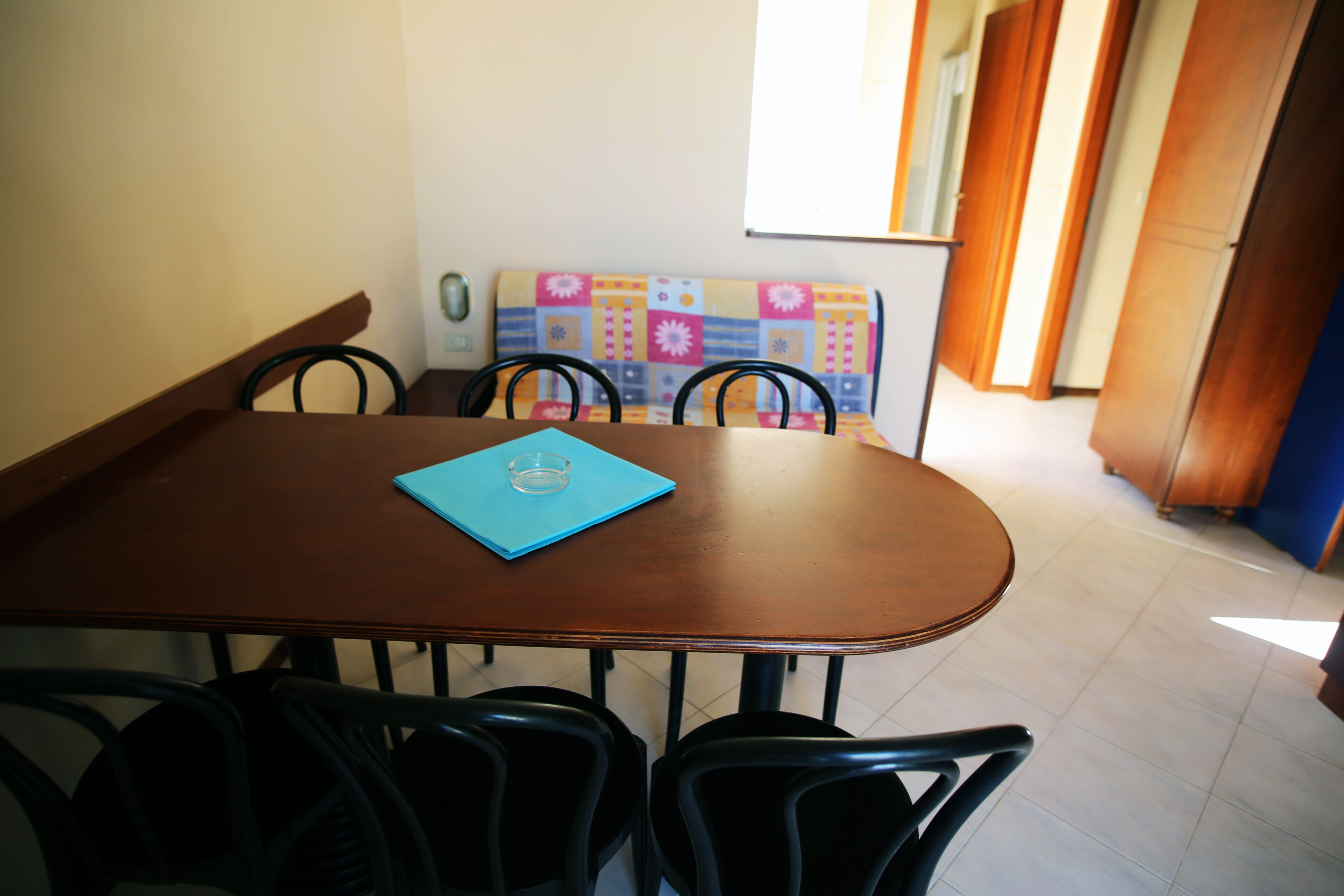 A dining area with a wooden table, four chairs, and a colorful bench in the background.