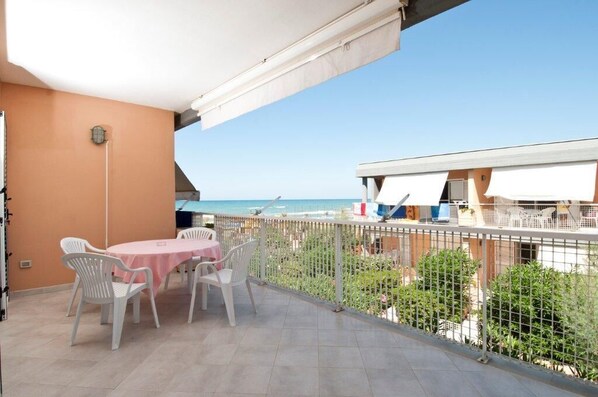A balcony with a table and chairs, overlooking a beach with umbrellas and a fence. - Blue Marine Village (Rodi Garganico)