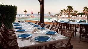 A dining area with tables set for a meal, overlooking a pool and beach. - Blue Marine Village (Rodi Garganico)
