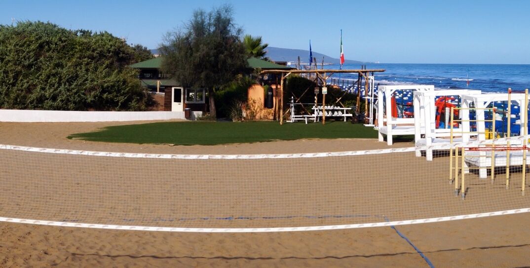 A beach volleyball court with a net, a small building with a green roof, and a flagpole.