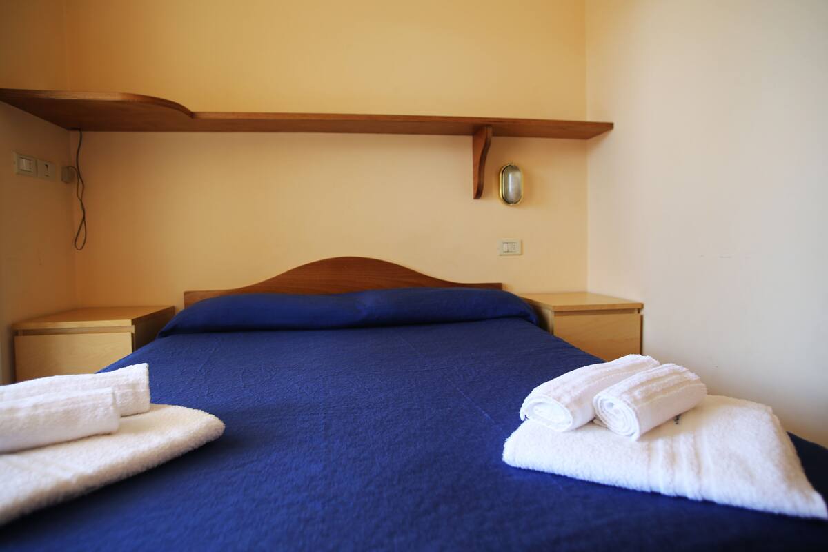 A neatly made bed with blue bedding and white towels, wooden headboard, and bedside tables.