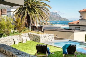 A pool area with two lounge chairs, a stone wall, and a view of the ocean and mountains. - Grand Camps Bay 5bed w Views Pool Gym Villa Serena (Cape Town)
