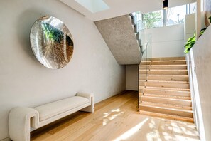 Un intérieur moderne avec un escalier en bois, un miroir rond et un banc.