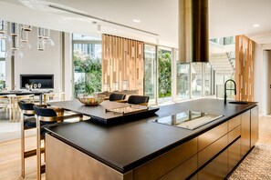 A modern kitchen with a large island, bar stools, and a dining area with a TV. - Grand Camps Bay 5bed w Views Pool Gym Villa Serena (Cape Town)