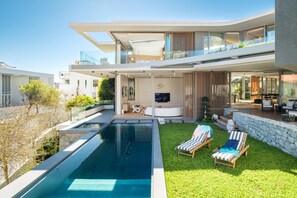 Une maison moderne à deux étages, dotée d’une piscine, d’un espace salon extérieur et d’un balcon.