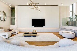 A modern living room with a flat-screen TV mounted on the wall, a sofa, a coffee table, and a large window.