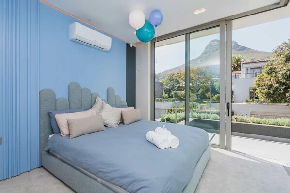 Un dormitorio moderno con una cama grande, vista a la montaña y un balcón con plantas.