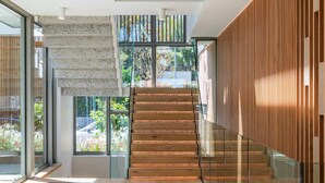 A modern staircase with glass railings, a wooden finish, and a view of greenery outside. - Grand Camps Bay 5bed w Views Pool Gym Villa Serena (Cape Town)