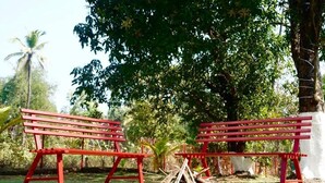 Due panchine rosse in un parco con alberi e un piccolo braciere al centro.