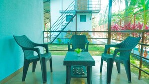 Un balcone con mobili in vimini e un tavolino, con vista su un giardino e un edificio con delle scale.