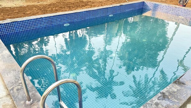 Una piscina rettangolare con bordo piastrellato in blu e una scala in metallo.