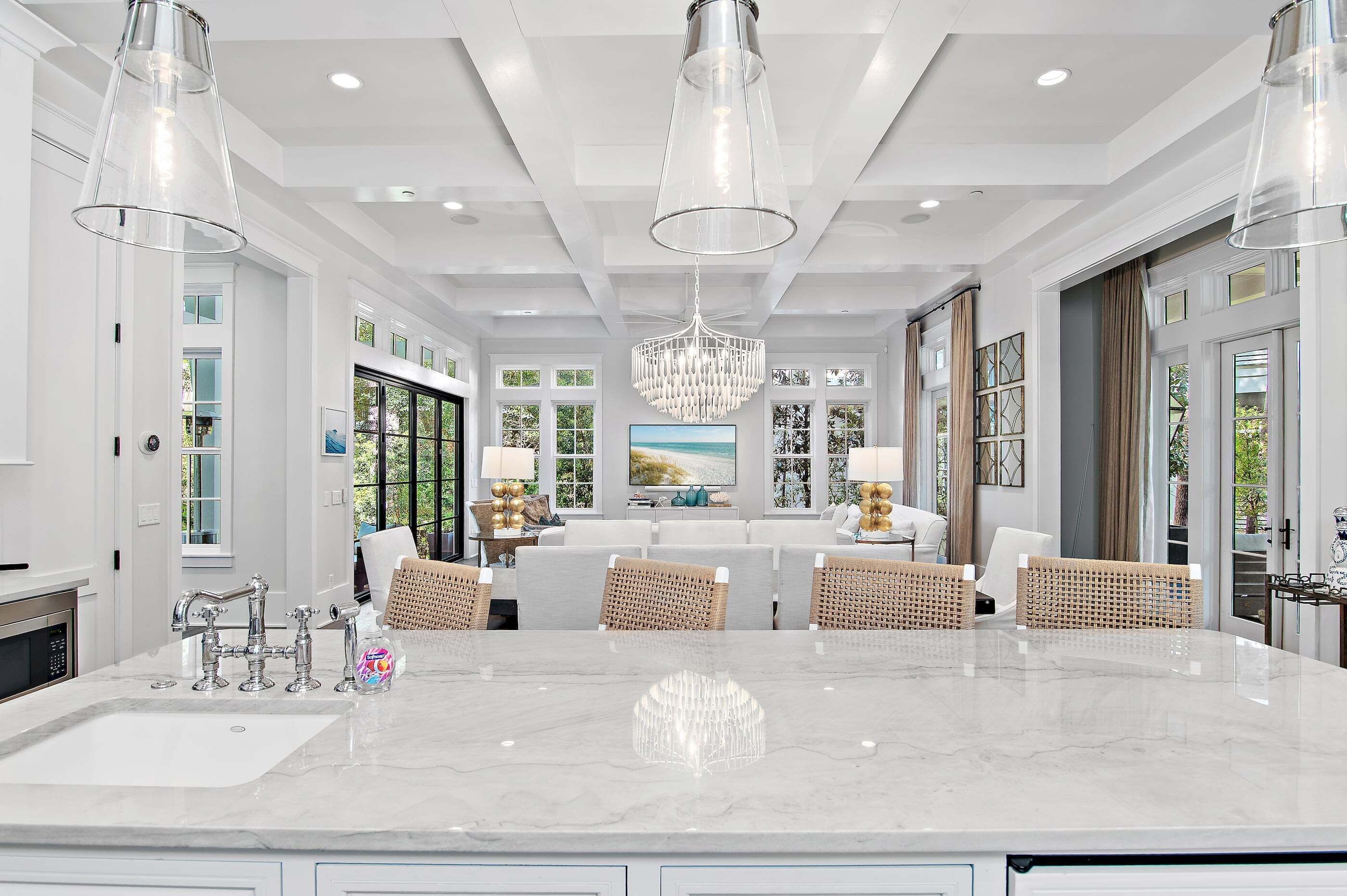 A spacious kitchen with a marble countertop, modern pendant lights, and a large chandelier.