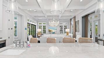 A spacious kitchen with a marble countertop, modern pendant lights, and a large chandelier.