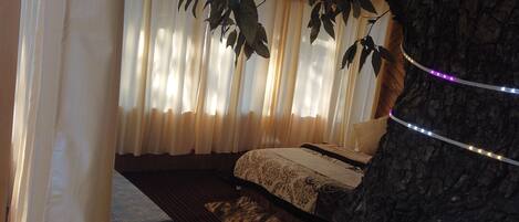 Un dormitorio con cama, cortinas y el tronco de un árbol.