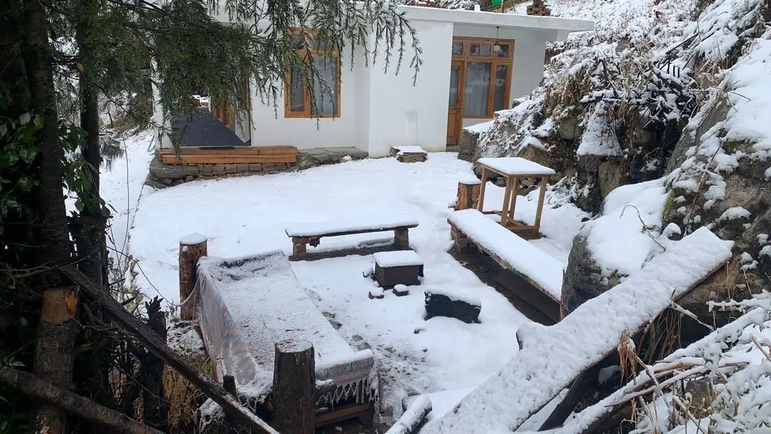 Un espace extérieur enneigé, avec un banc en bois, une table de pique-nique et un mur en pierre.