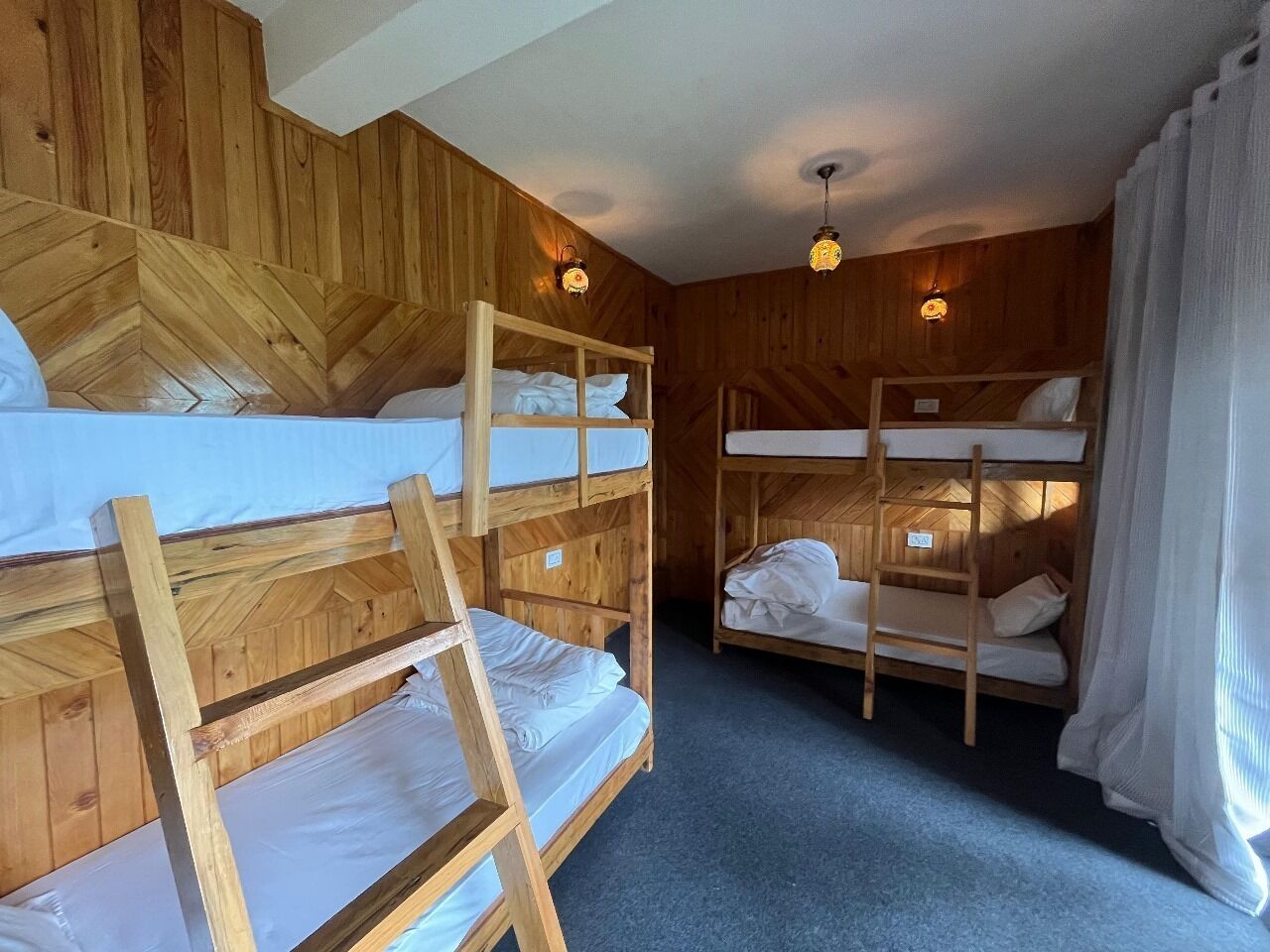 A bunk bed room with wooden walls and ceiling, two bedside lamps, and a blue carpet.