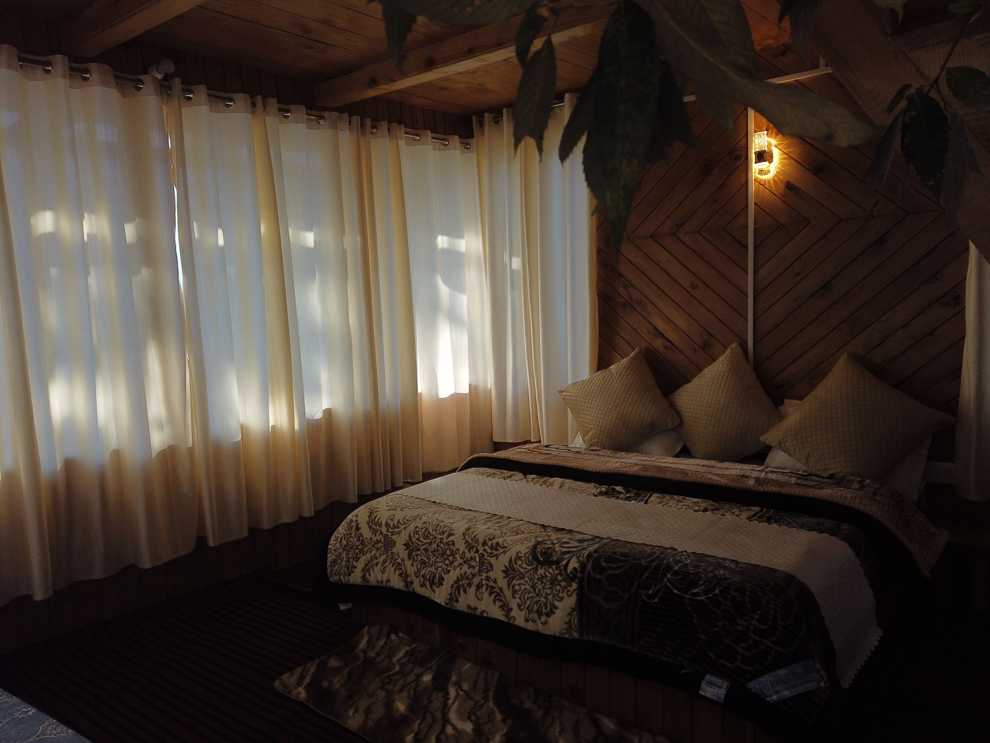 A bedroom with a wooden ceiling, a bed with patterned bedding, and sheer curtains.