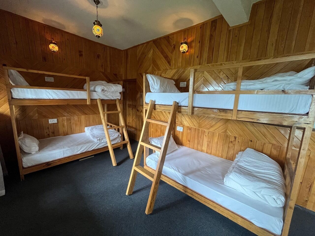 A room with bunk beds, wooden walls, and two wall-mounted lights.