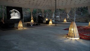 A tented outdoor area with a large screen displaying a bird, surrounded by cone-shaped lights and a red carpet. - The Isisinga (Banjar)
