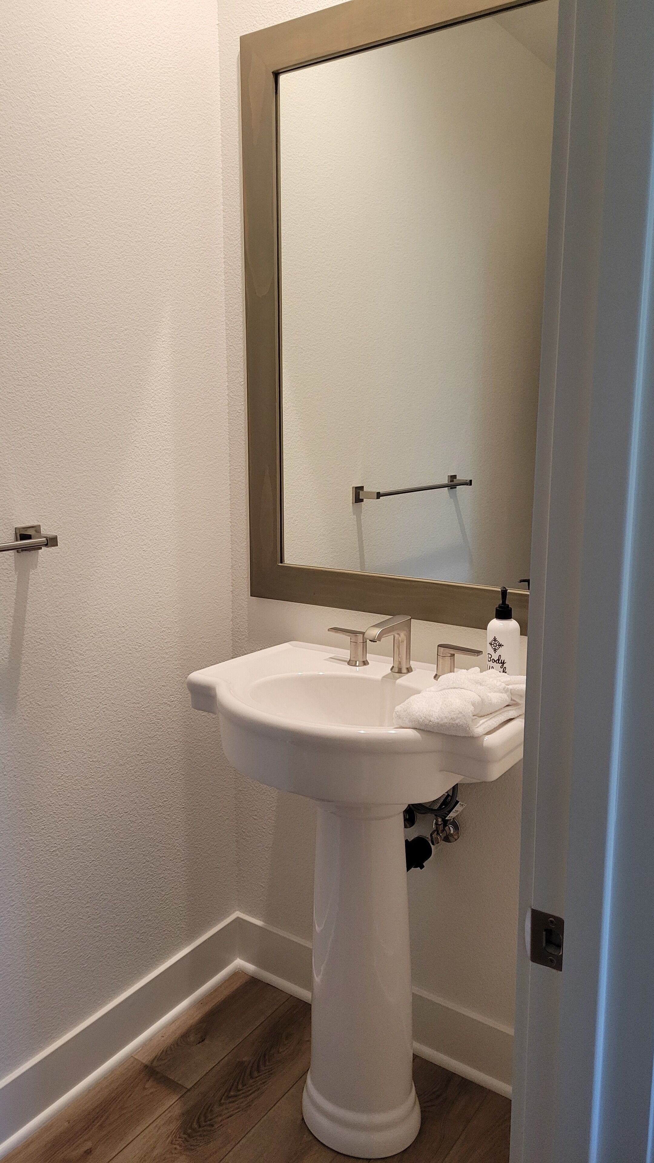 Un baño con un lavamanos pedestal blanco, un espejo y un perchero para toallas.