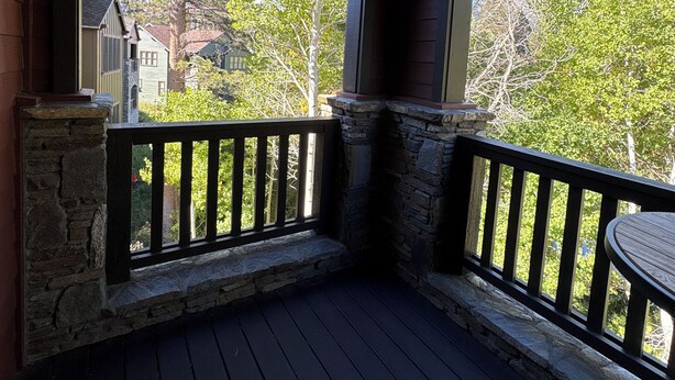 A wooden deck with stone railings and a view of a neighborhood. - Snowcreek Resort Vacation Rental 1555 (Mammoth Lakes)