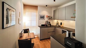 A modern kitchen with a dining area, featuring a wooden table, chairs, a coffee machine, and a built-in microwave.