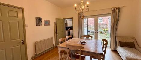 A dining area with a wooden table and chairs, a chandelier, and a view of a garden through a glass door.