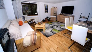 A living room with a sofa, a dining table, a TV, and a kitchen area.