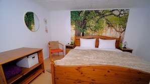 A bedroom with a wooden bed, a nightstand, a chair, a shelf, and a tapestry of trees on the wall.