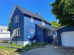 A two-story house with a blue exterior, a visible garage door, and a ladder leaning against the house. - Best location in the Keewenaw! (Mohawk)