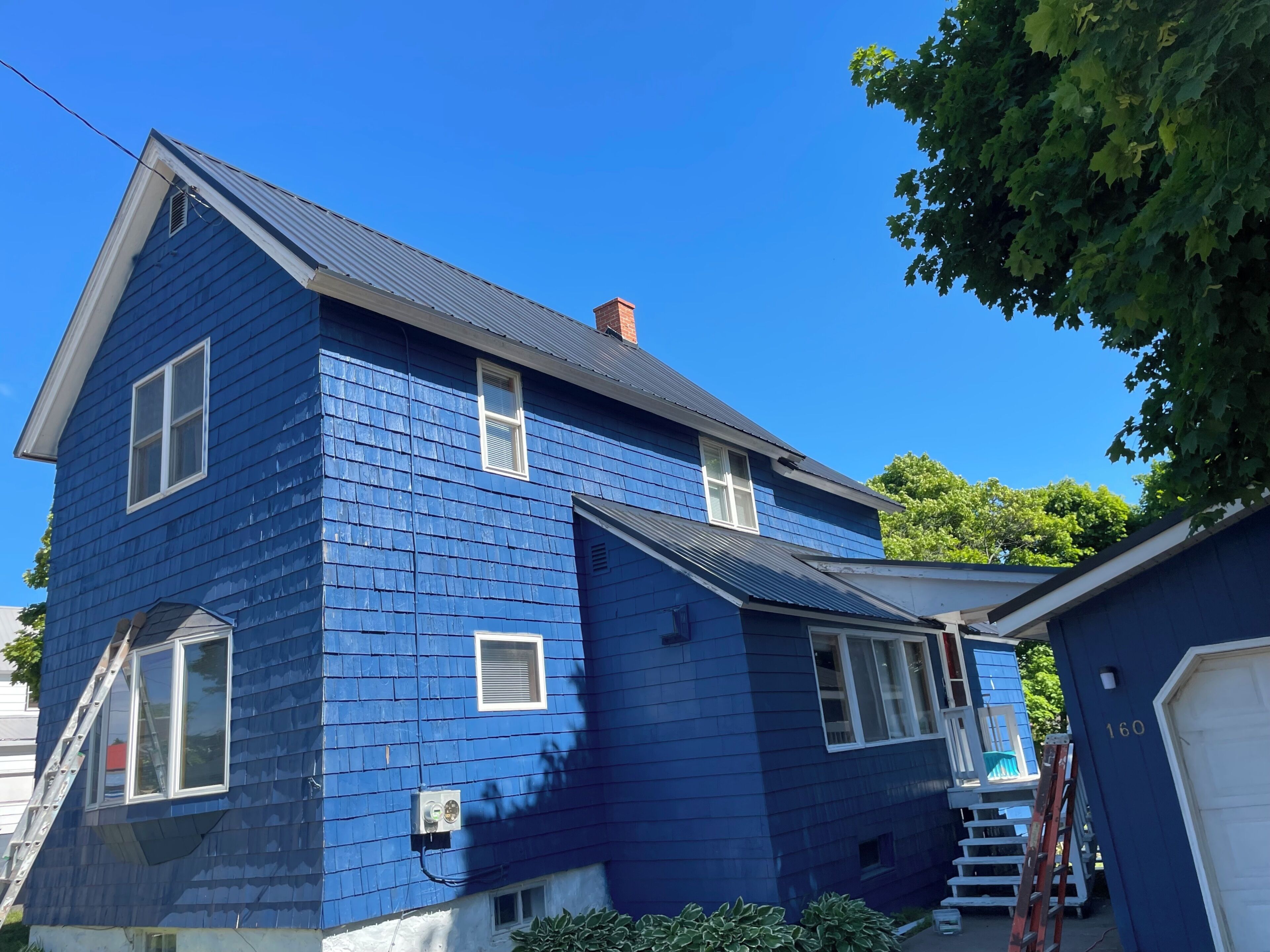 A two-story house with a blue exterior, a visible chimney, and a garage with the number 160.