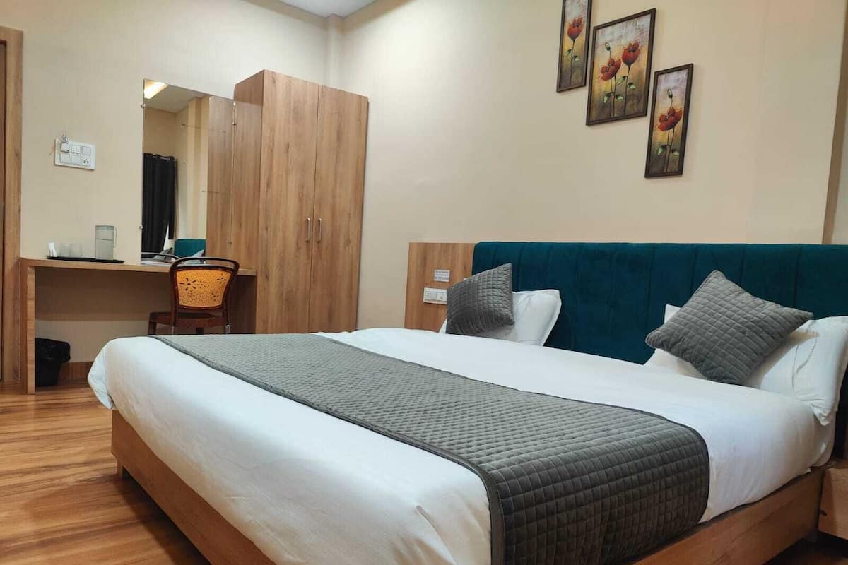 A hotel room with a large bed, a desk with a chair, and a wardrobe.