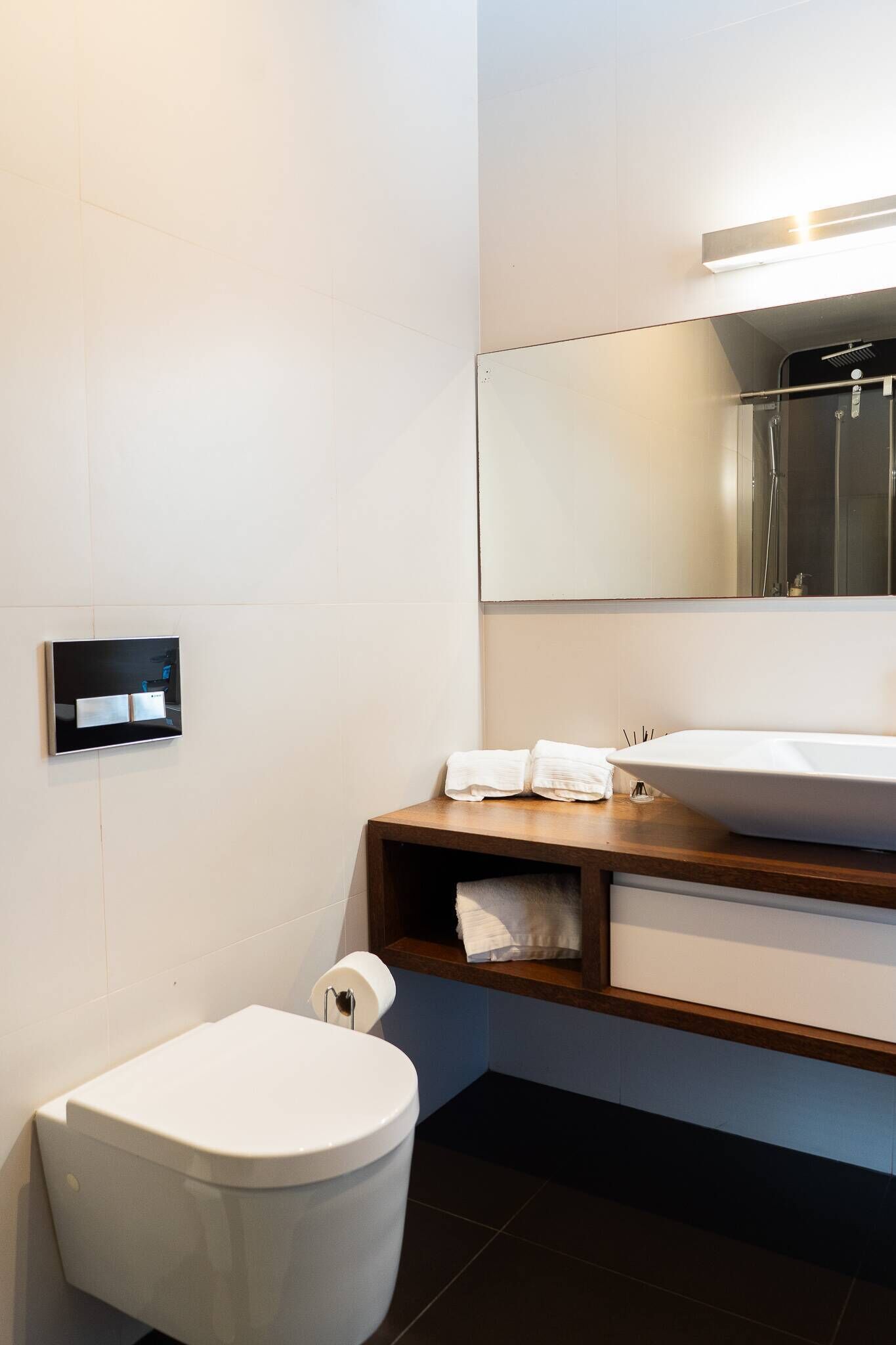 Un baño moderno con un inodoro blanco, un tocador de madera con un lavamanos grande y un espejo sobre el tocador.