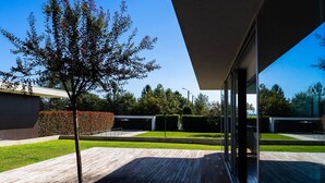 Een modern gebouw met een glazen gevel, een houten terras en een verzorgd gazon.