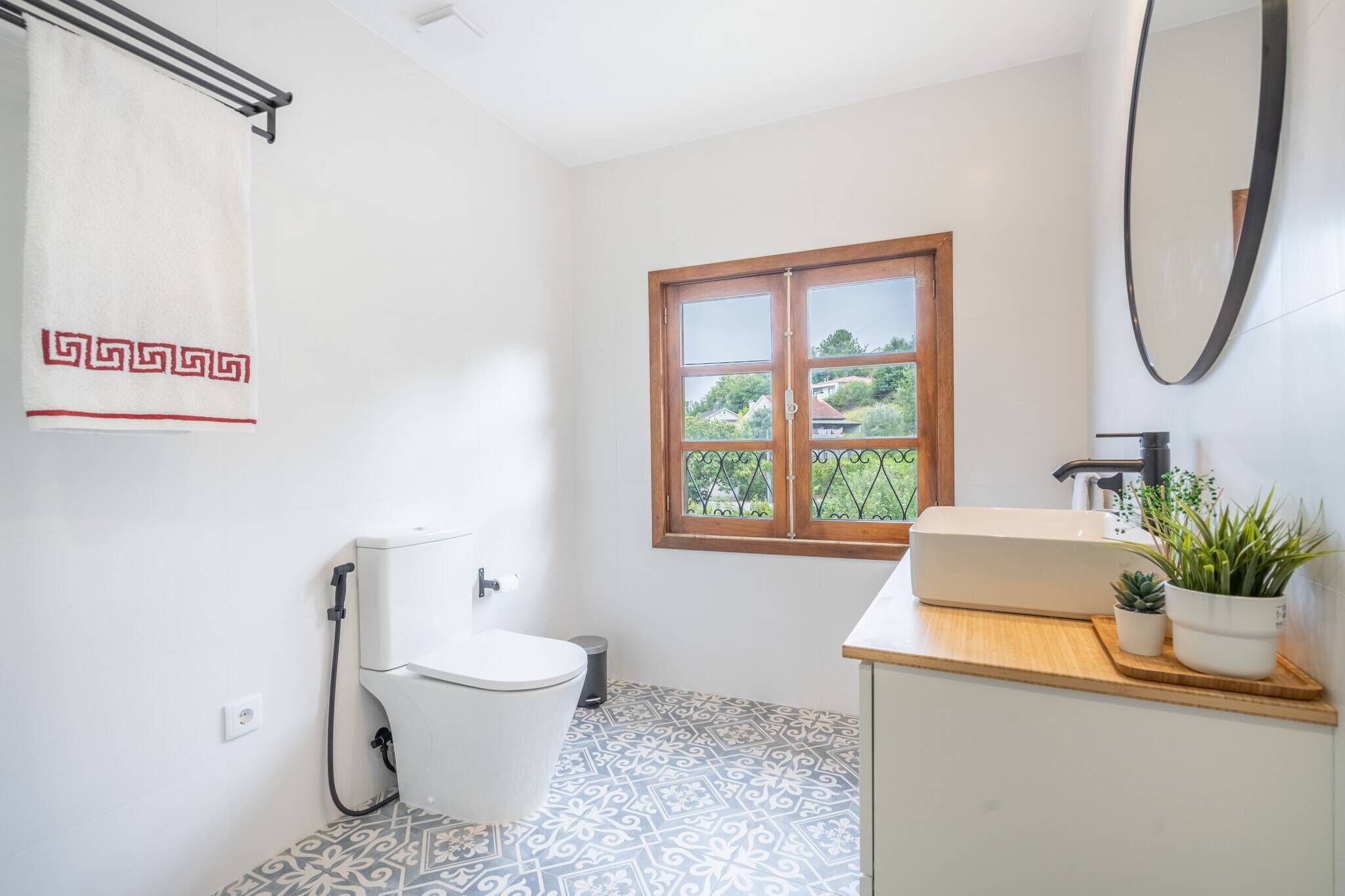 Ein Badezimmer mit Toilette, Waschbecken, Fenster mit Blick auf Grünflächen und einem Spiegel.