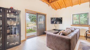 Un salon moderne avec un plafond en bois, une vitrine, un canapé, un téléviseur et une grande fenêtre donnant sur un paysage verdoyant.