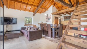 Un salon chaleureux avec un plafond en bois, un canapé, un téléviseur et un escalier.
