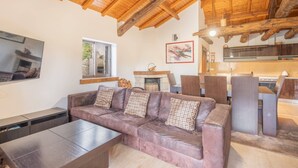 Un salon moderne avec un canapé en cuir, des poutres apparentes en bois au plafond, une cheminée et un coin cuisine.