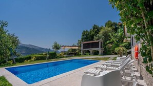 En swimmingpool med solstolar, en livboj och utsikt över kullar.