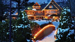 Une grande maison en bois à plusieurs étages, avec une allée enneigée et un pont illuminé.