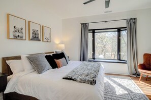A bedroom with a bed, a nightstand, a chair, a window with curtains, and wall art.