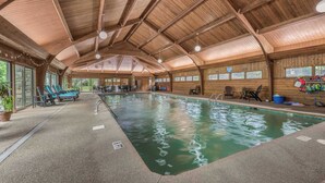 Une piscine intérieure aux murs et au plafond en bois, entourée de chaises longues et de tables.