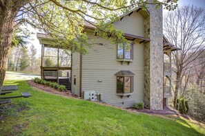 A two-story house with a stone chimney, a covered porch, and a small deck.