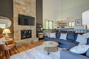 A modern living room with a stone fireplace, a large sofa, and a flat-screen TV mounted on the wall. - Condo 3B/3BA + Amenity Pass w/ Hot Tub + Pool. (Blowing Rock)
