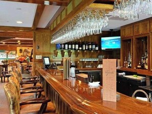 Eine Bar mit Holzbalken, verschiedenen Sitzmöglichkeiten und einem Fernsehbildschirm.