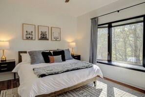 Ein Schlafzimmer mit einem großen Bett, Nachttischlampen, gerahmten Bildern an der Wand und einem Fenster mit Vorhängen.