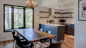 Une cuisine moderne dotée d’un îlot central, d’appareils électroménagers intégrés et d’une grande fenêtre donnant sur une forêt.