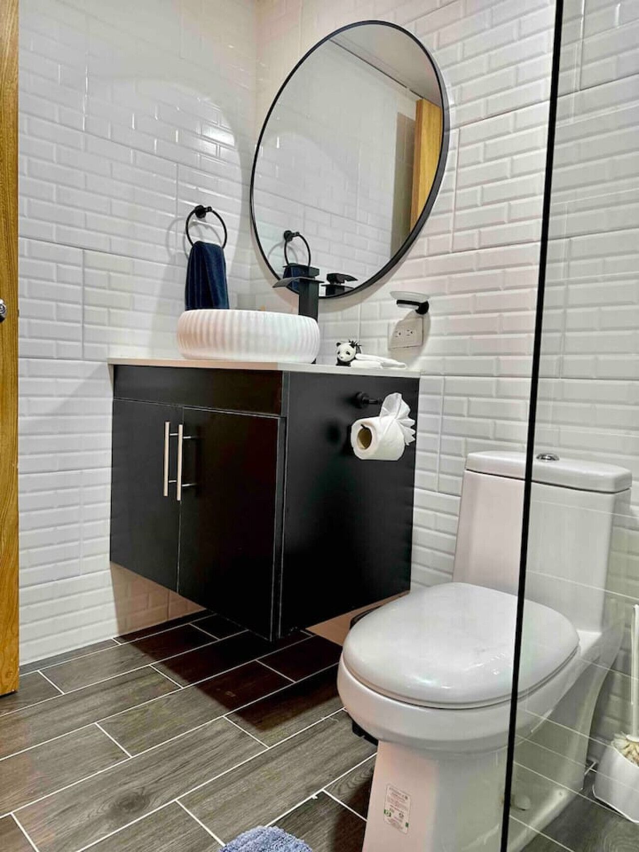A modern bathroom with white subway tiles, a black vanity, a white toilet, and a round mirror.