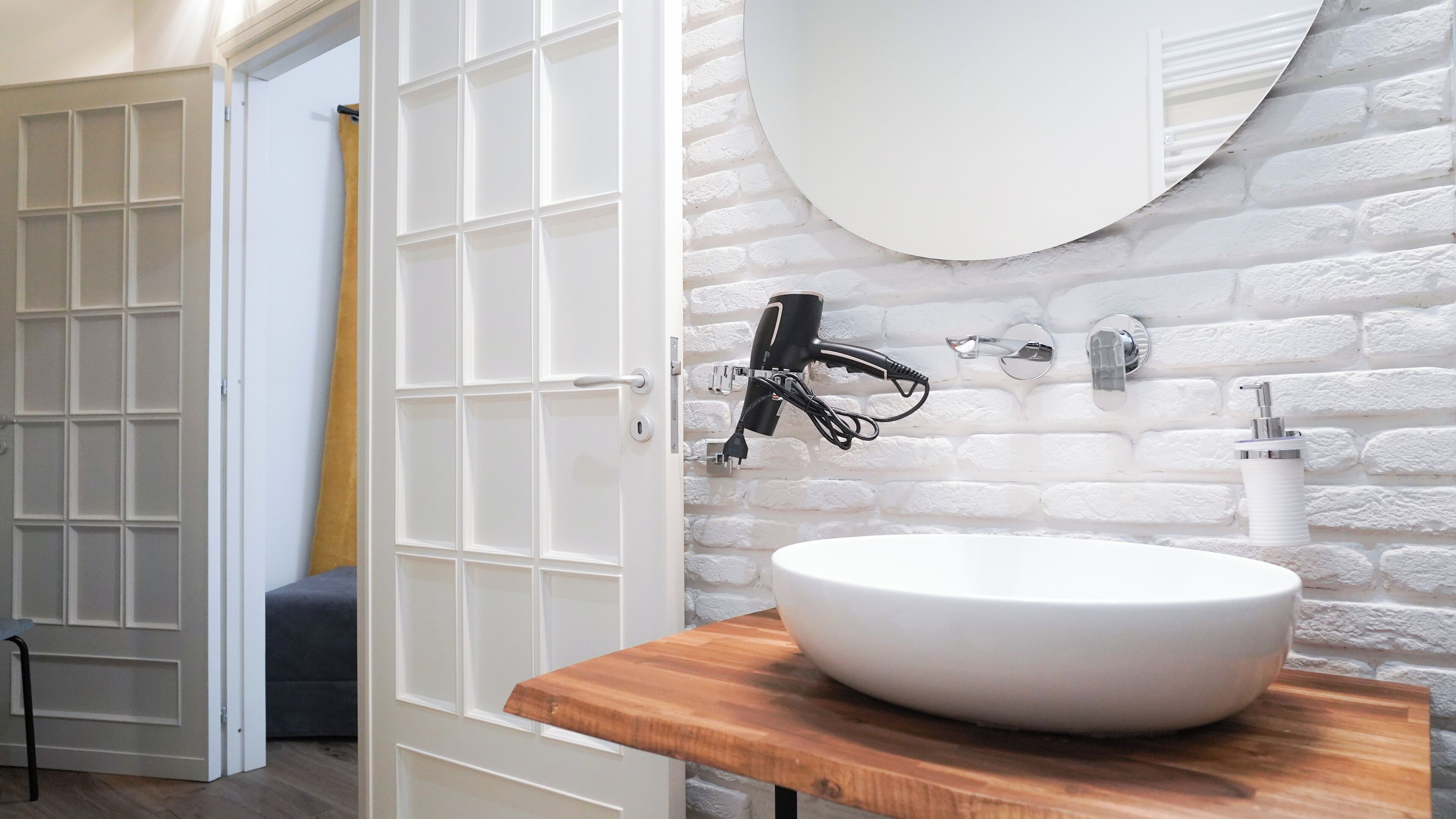 A bathroom with a white sink, a round mirror, and a hairdryer mounted on the wall.