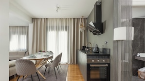 A modern kitchen with a built-in oven, a dining area with a round table and chairs, and a living area with a sofa and curtains. - Anvy Stylish Suites Ioannina (Ioannina)